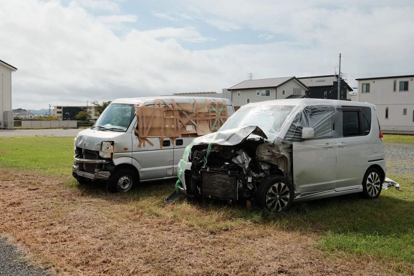 Two silver minivans with crushed front ends parked on grass in a residential area