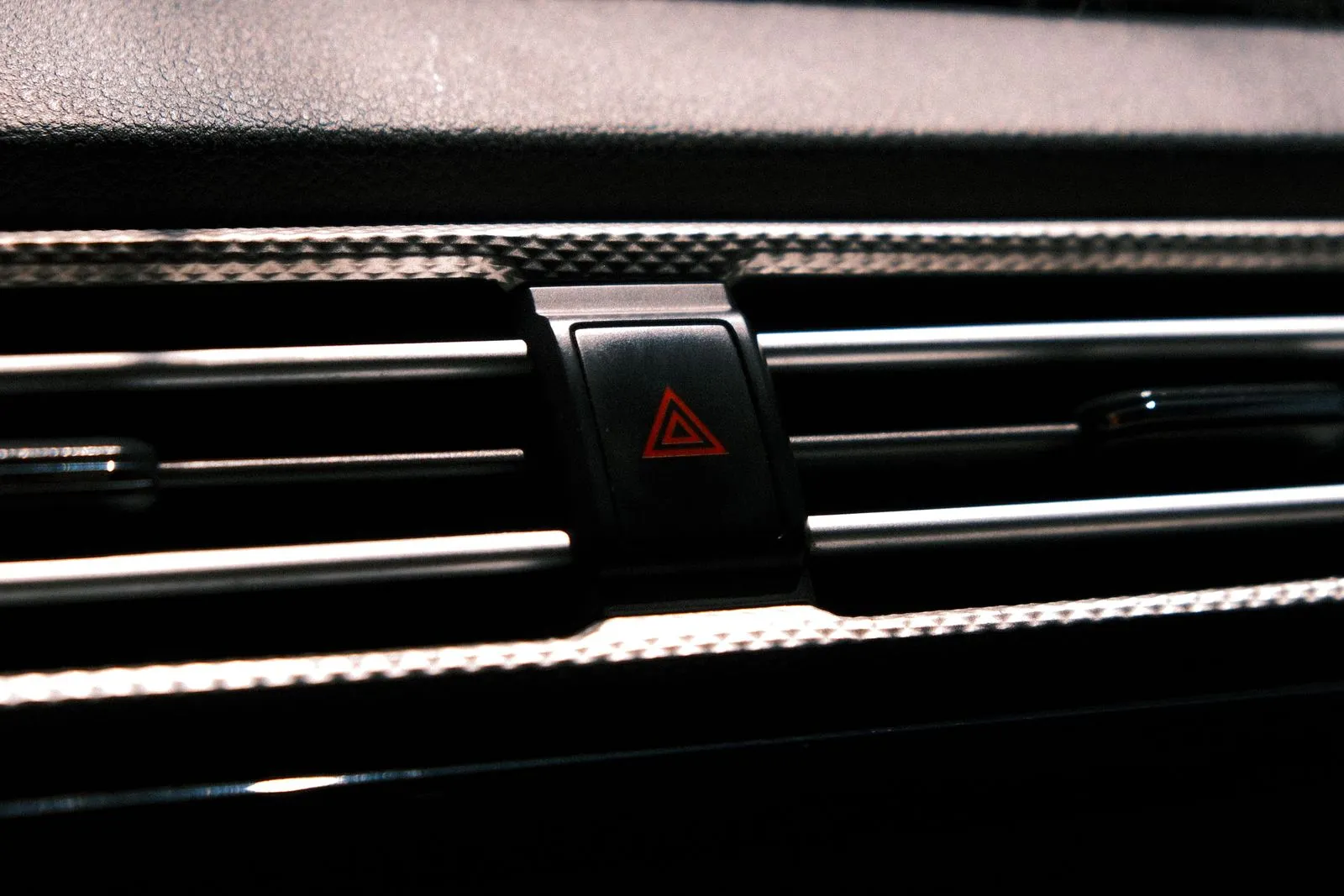Close-up of a car's hazard light button with a red triangle on the dashboard
