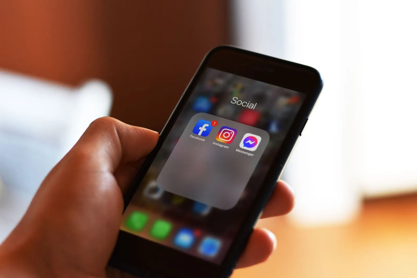 Una mano tiene uno smartphone con una cartella che contiene le app Facebook, Instagram e Messenger