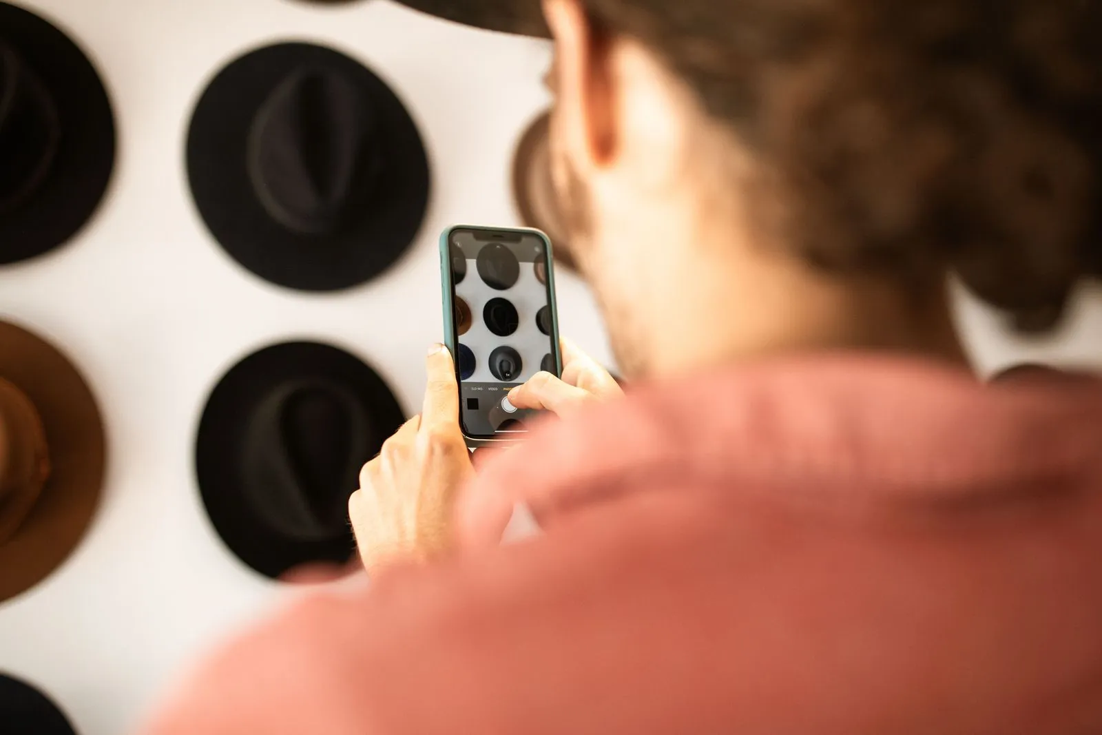 Persona che fotografa con lo smartphone dei cappelli appesi a una parete