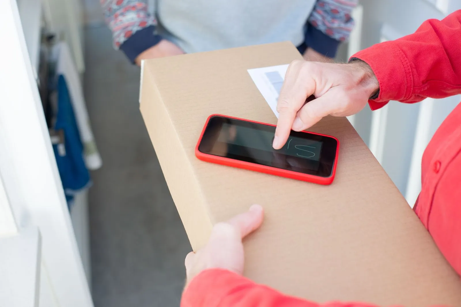 Hands tapping a smartphone that rests on a cardboard parcel at a front door
