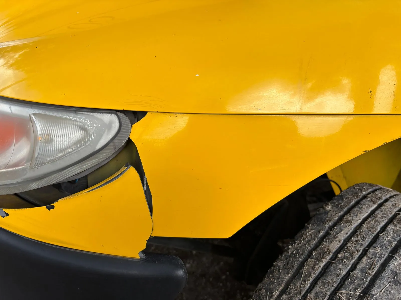 Pannello giallo della carrozzeria incrinato sotto un faro, con uno pneumatico nell'angolo