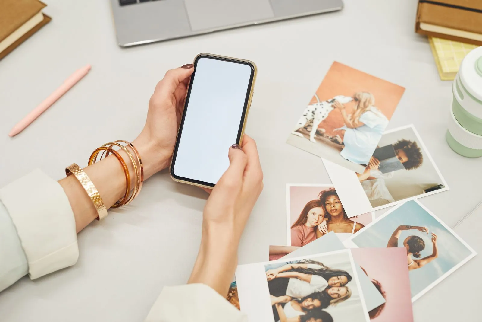Mani che tengono uno smartphone sopra un tavolo con foto stampate e un portatile