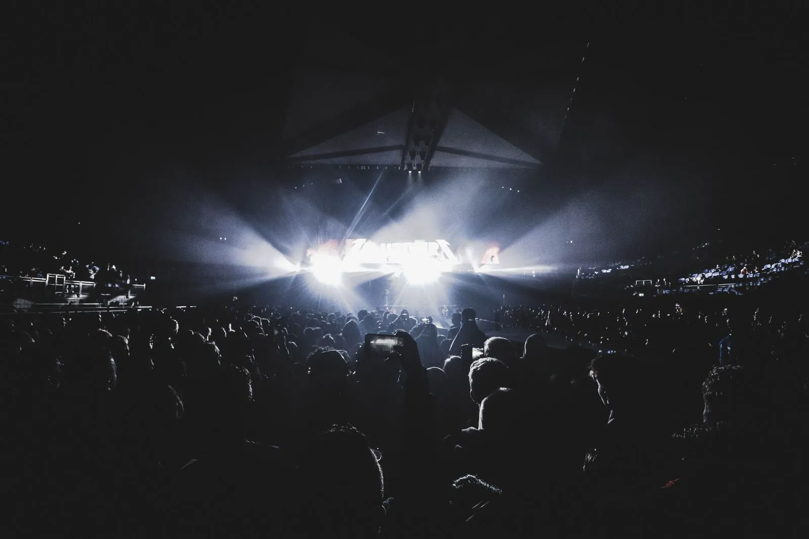 Público numa arena escura assiste a um palco muito iluminado