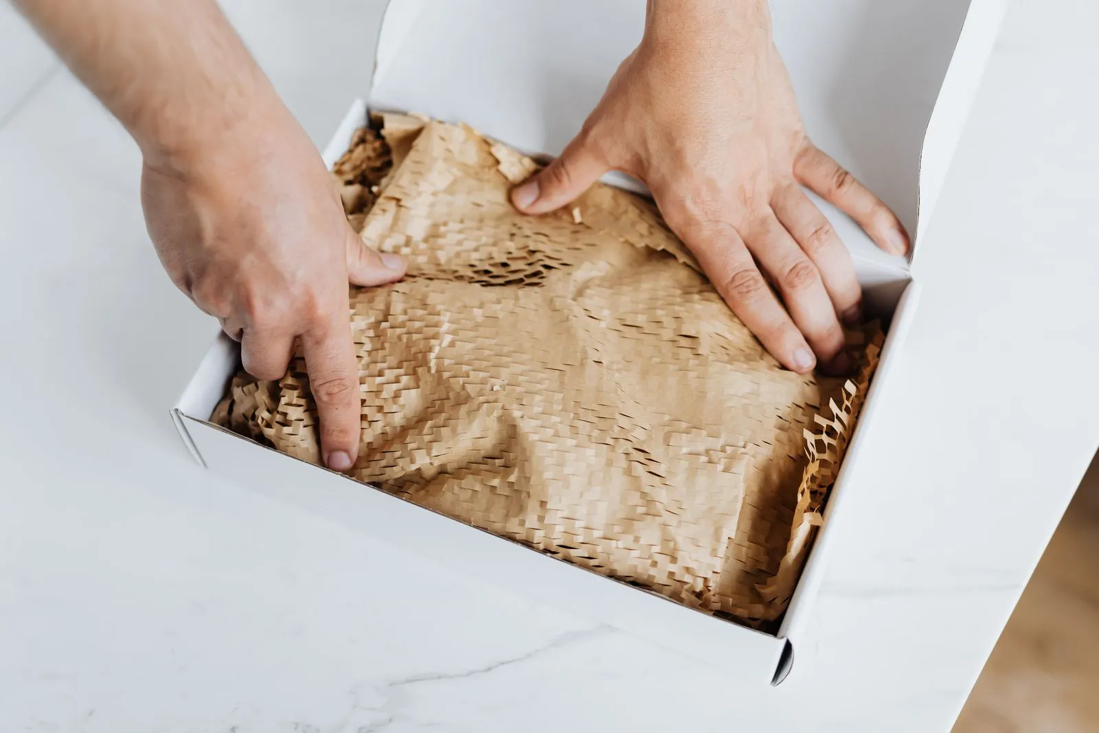 Two hands press paper padding into a white shipping box